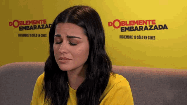 a woman is crying in front of a sign that says doblemente embarazada