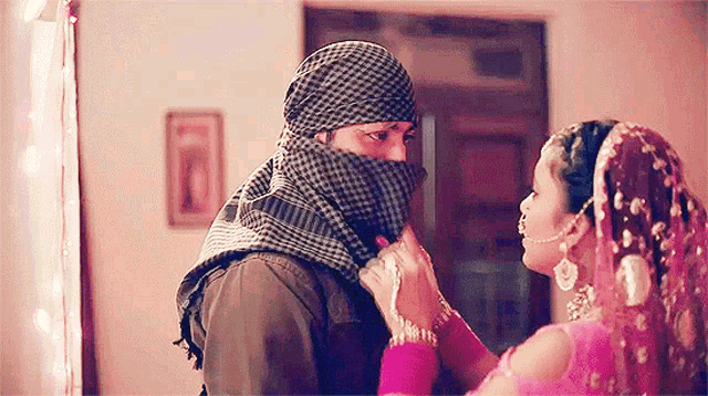 a man wearing a scarf covering his face is kissing a woman in a pink dress .