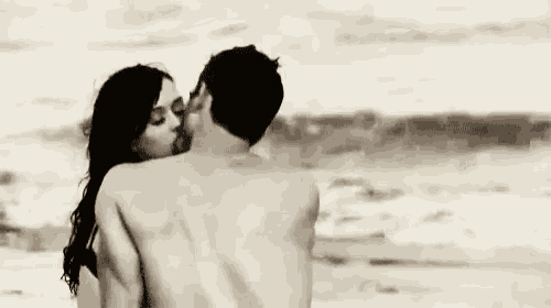 a black and white photo of a man and woman kissing on the beach .