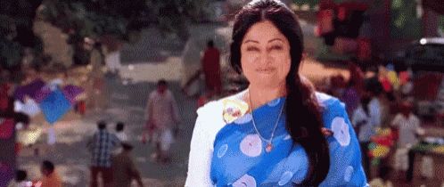 a woman in a blue saree is standing in front of a crowd of people on a street .