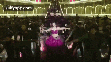 a woman in a pink dress is dancing on a stage in front of a crowd .