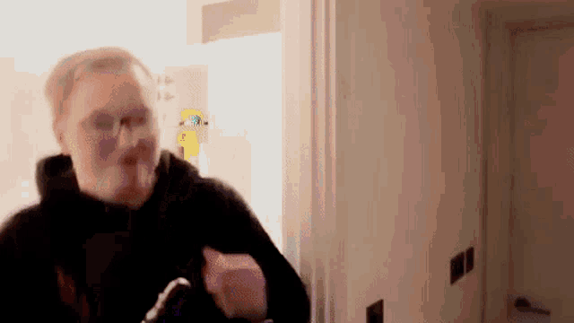 a man in a black hoodie is standing in a room with a white door .