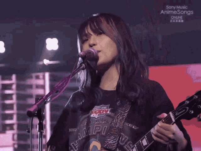 a girl is singing into a microphone while holding a guitar and wearing a shirt that says campion on it