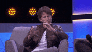 a man in a leather jacket is sitting in a chair talking
