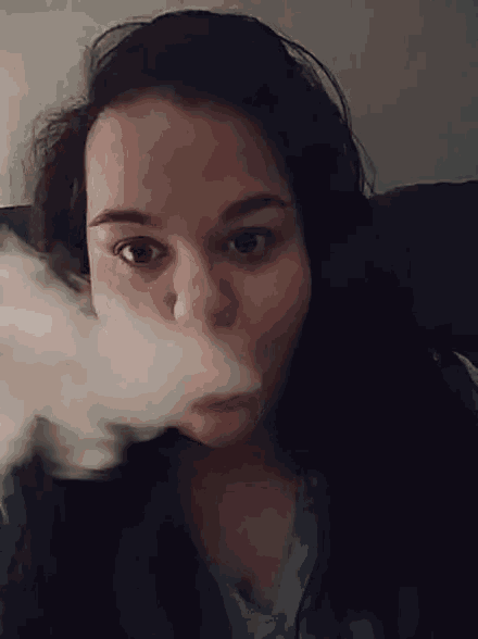 a woman in a blue shirt is blowing smoke from her mouth
