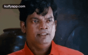 a man in a red shirt is making a funny face while looking at the camera .