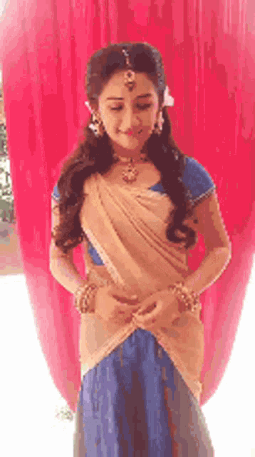 a woman in a blue and gold dress is standing in front of a red curtain and smiling .
