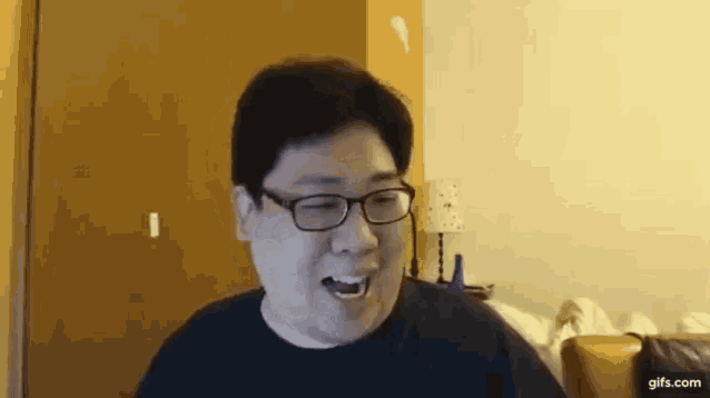 a man wearing glasses and a black shirt is sitting on a couch in a living room .