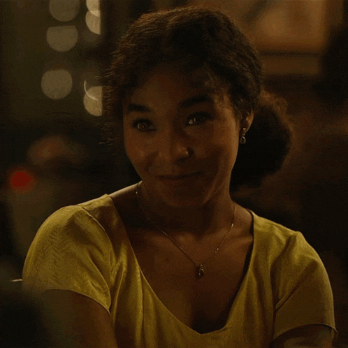 a woman wearing a yellow top and a necklace smiles