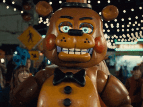 a stuffed teddy bear wearing a bow tie is standing in front of a crowd