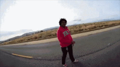 a man wearing a red hoodie that says fly is standing on the side of a road .