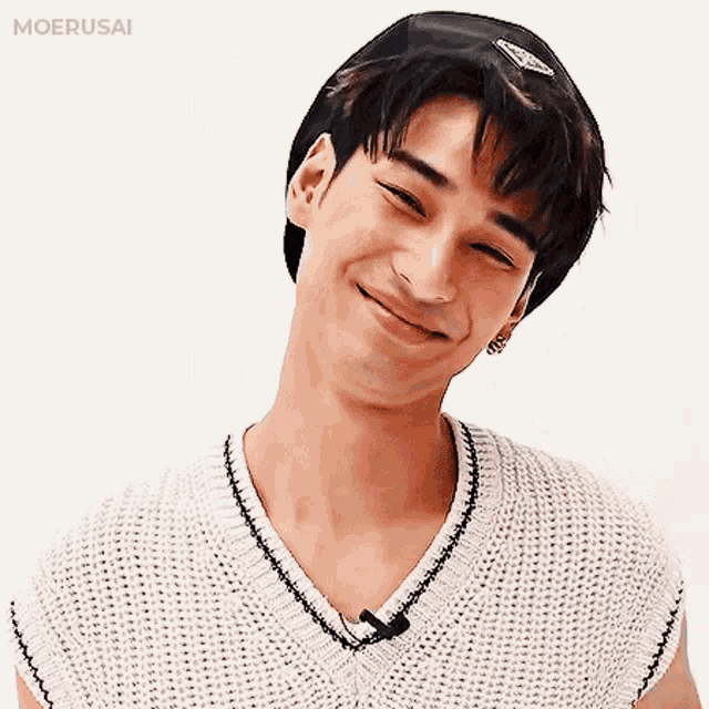a young man wearing a white sweater and a hat is smiling .