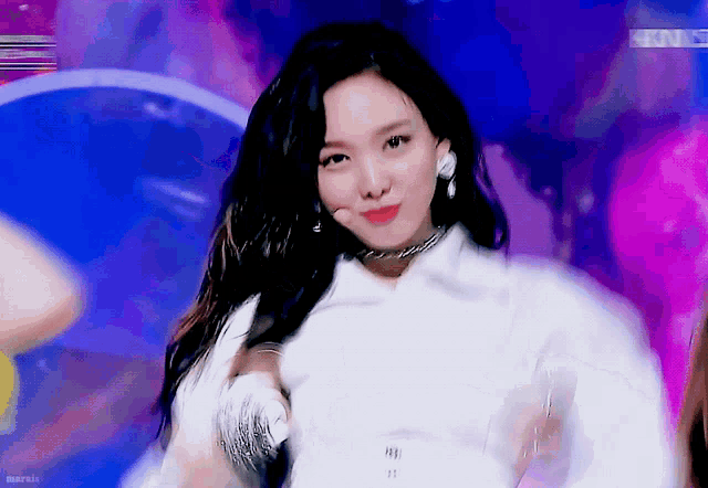 a woman with long black hair is wearing a white shirt and earrings while dancing on a stage .