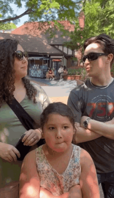 a little girl making a funny face while standing next to a man and a woman