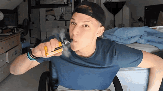 a young man is smoking an electronic cigarette in a bedroom