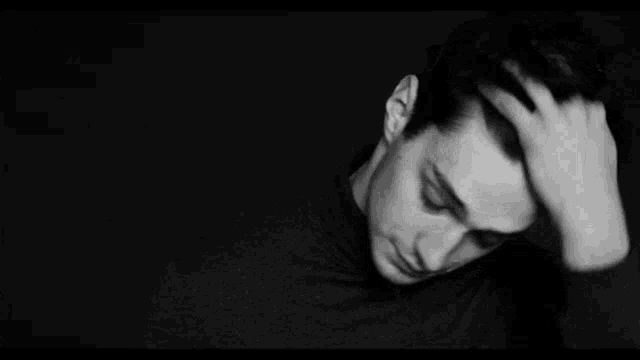 a black and white photo of a man in a turtleneck sweater looking down .