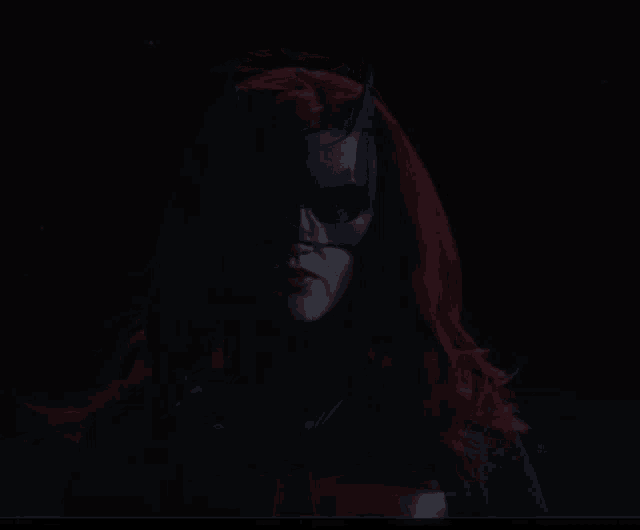 a woman with red hair wearing a batman mask