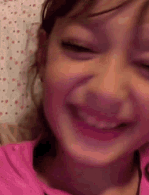 a little girl in a pink shirt is smiling with her eyes closed and her mouth open .