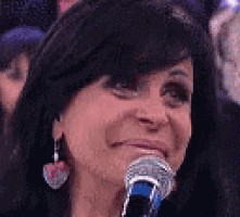 a woman is smiling while holding a microphone in front of a crowd .