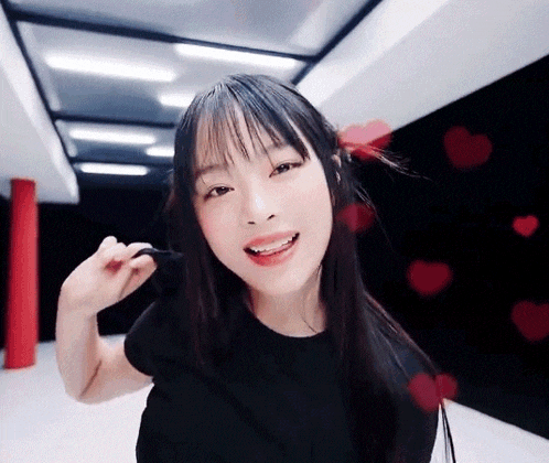 a woman in a black shirt is smiling and looking at the camera with red hearts flying around her .