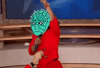 a person wearing a green mask and a red shirt is holding a microphone
