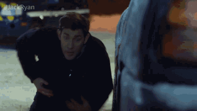 a man is kneeling next to a car with #jackryan written above him