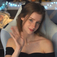 a woman in a black off the shoulder top is sitting in a chair and waving her hand .