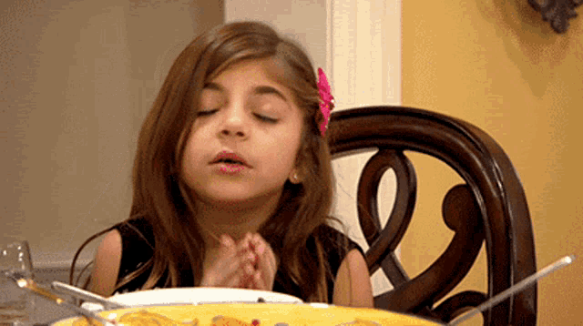 a little girl is sitting at a table with a plate of food and a spoon .