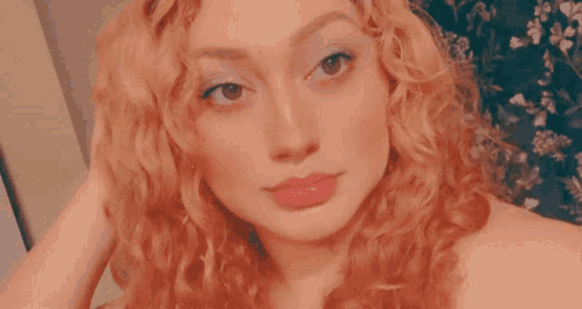 a woman with curly hair is taking a selfie in front of a floral curtain