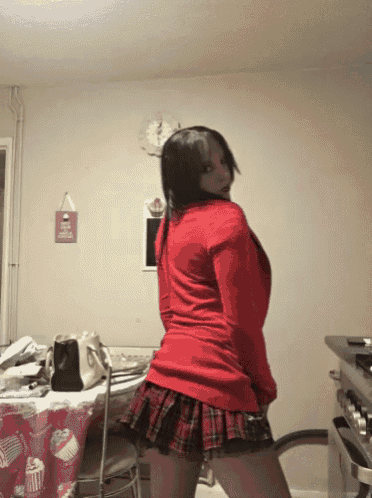 a woman in a red sweater and plaid skirt stands in front of a sign that says cupcakes