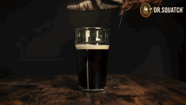 a hand holding a glass of beer with dr.squatch written in the corner