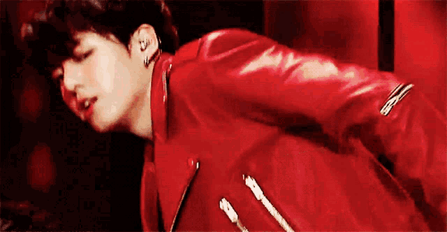 a man wearing a red leather jacket and earrings is dancing on a stage .