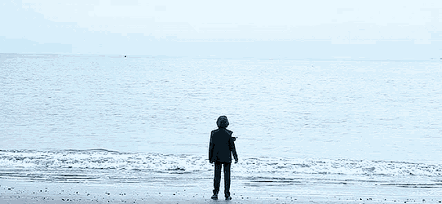 a man in a suit is standing on a beach looking out over the ocean