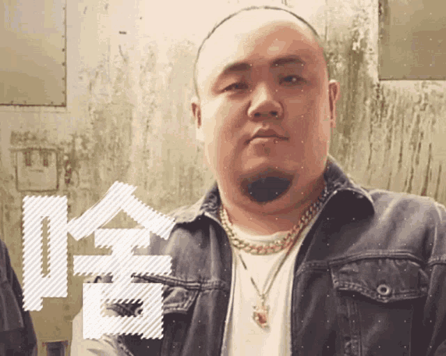 a bald man with a beard wearing a denim jacket and gold chains