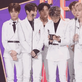 a group of young men in white suits are standing in front of microphones on a stage