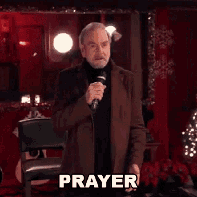 a man with a beard is holding a microphone and saying `` prayer '' while standing in front of a guitar .
