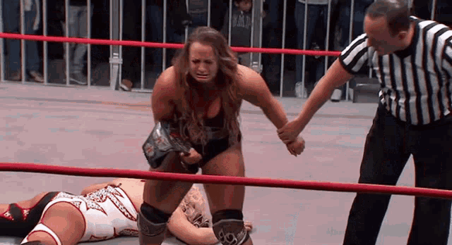 a woman in a wrestling ring holds the hand of a referee while another woman lays on the ground