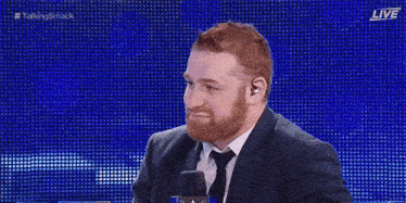a man in a suit and tie is sitting in front of a microphone and waving .