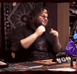 a man with a beard is sitting at a table with his fist up