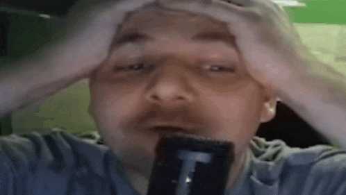 a man is holding his head in his hands while holding a microphone .
