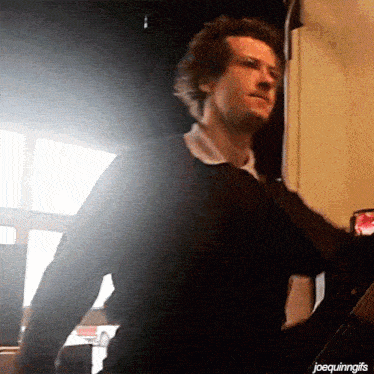 a man in a black shirt is standing in front of a window with the words joequinngifs below him