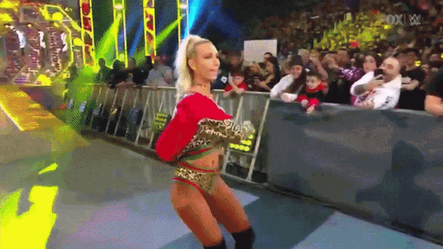 a woman in a leopard print outfit is dancing in front of a crowd at a wrestling show