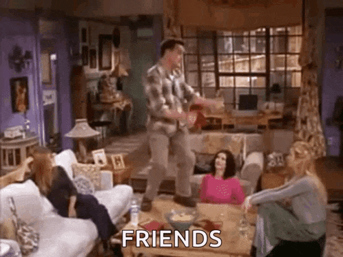 a man is dancing in a living room with a group of people sitting on couch .
