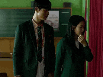 a man and a woman are standing next to each other in a classroom in front of a blackboard .