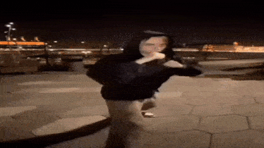 a man in a black hoodie is standing on a sidewalk at night holding a microphone .