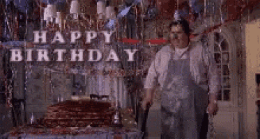a man is standing in front of a birthday cake in a room with balloons and streamers .