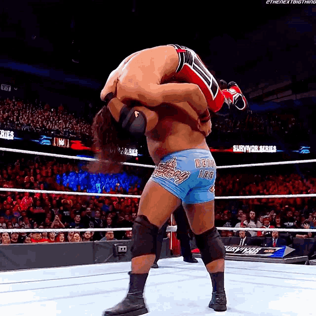a wrestler wearing blue shorts with the word deuce on them is being lifted by another wrestler