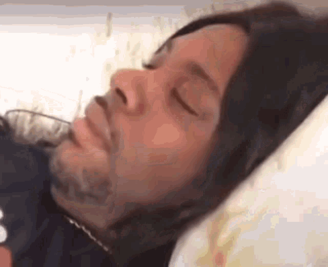 a man is laying in bed with his eyes closed .