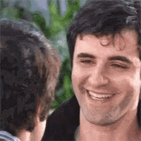 a man with a tattoo on his forehead is smiling while looking at another man .