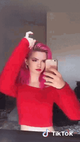 a woman with pink hair is taking a selfie in front of a mirror with a tiktok logo on the bottom